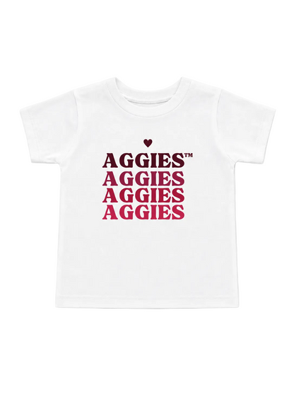 A white short-sleeve kids' t-shirt featuring a graphic print on the front with the word 'AGGIES' repeated in stacked rows, starting with a small dark red heart above the first line.